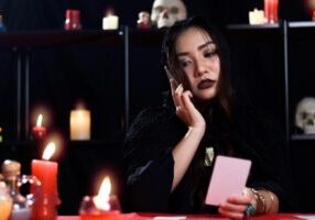 Mysterious magnificent beautiful woman fortune teller in black hood read future on card and calling to customers to tell them, online working running business.